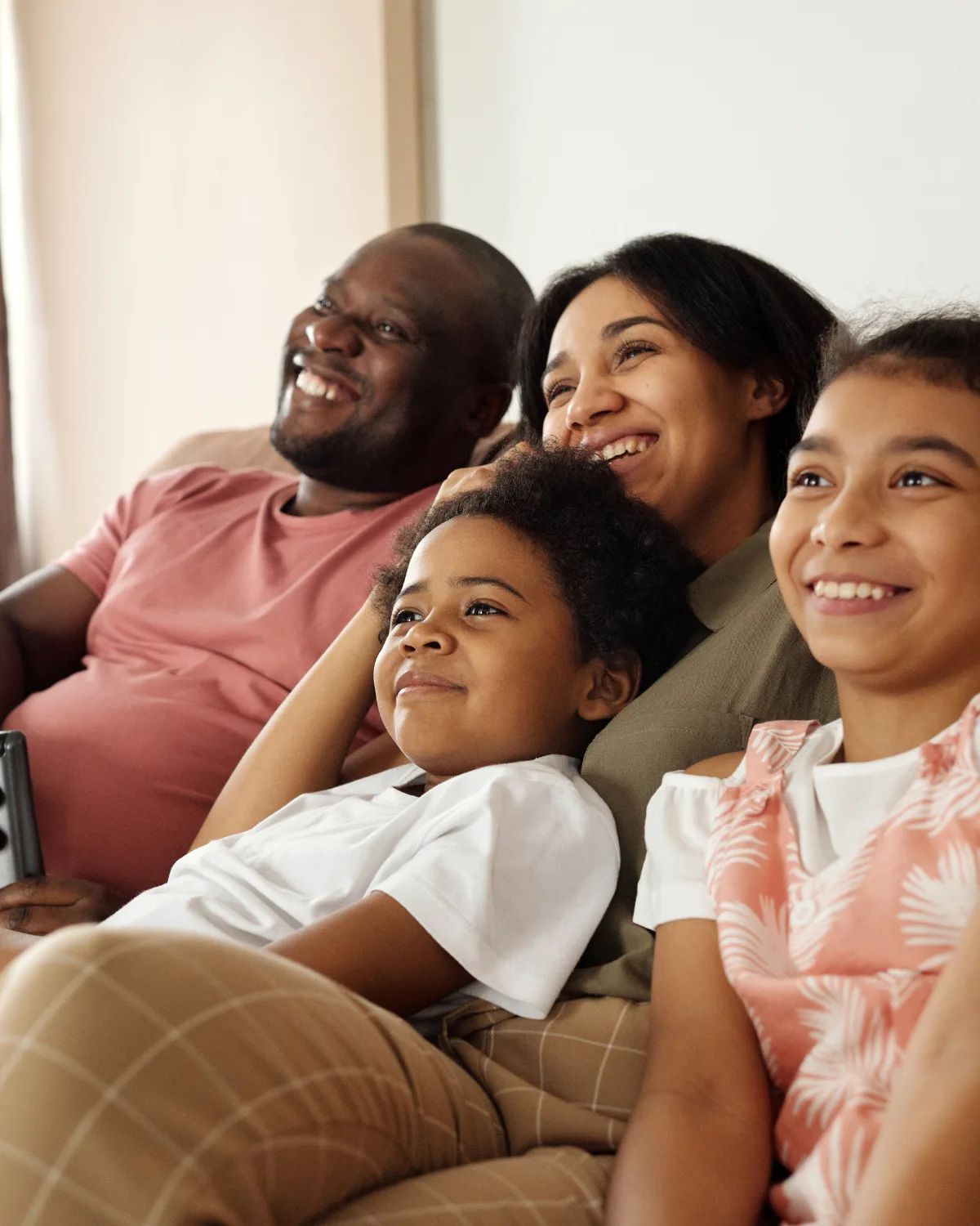 A family of four — two parents and two children — relaxing together on a couch, smiling and at ease