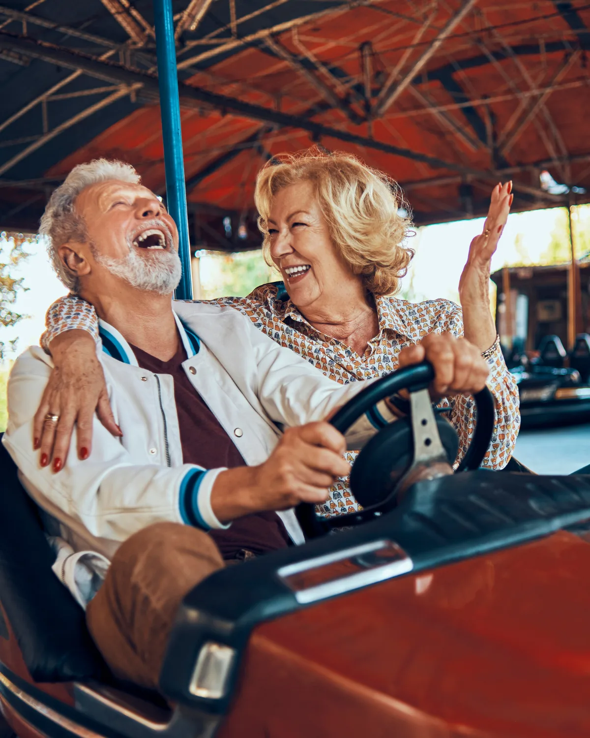 A retired couple laughing together while riding a bumper car, enjoying their retirement years