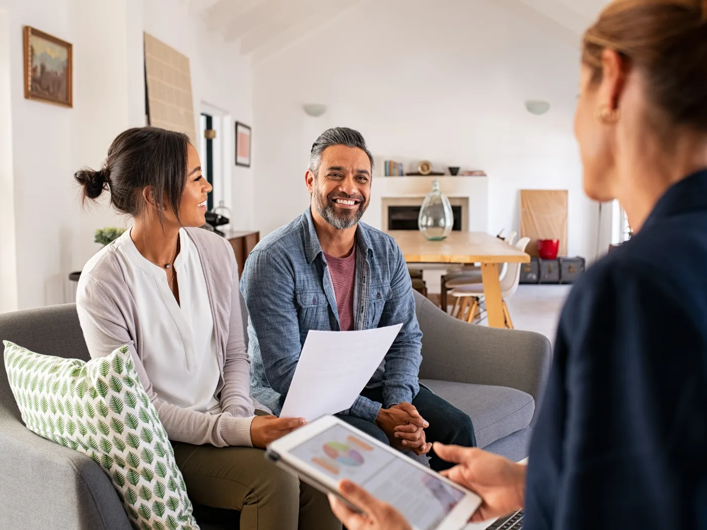 An FCPC agent reviewing a financial plan on a tablet with a smiling couple in their living room