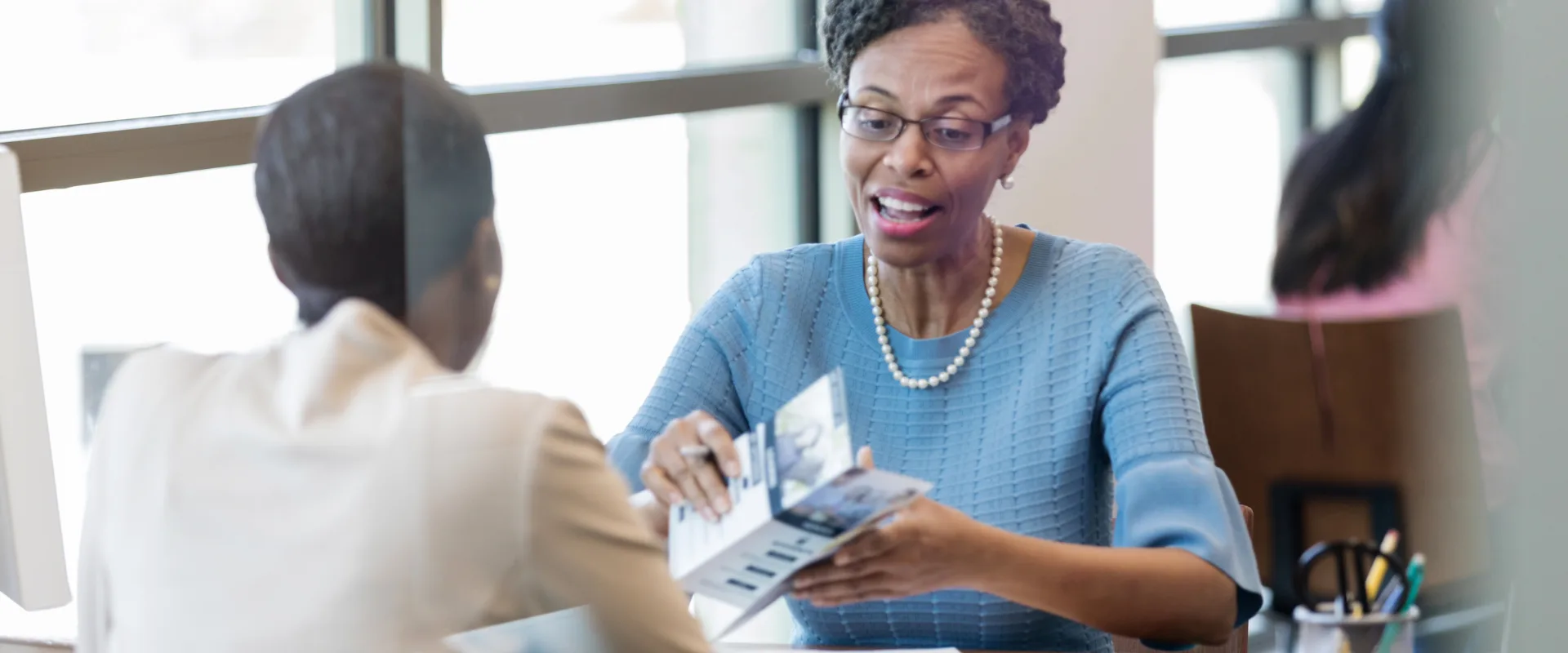 An FCPC agent leaning forward and showing a brochure to a client seated across the table, engaged in a warm professional conversation
