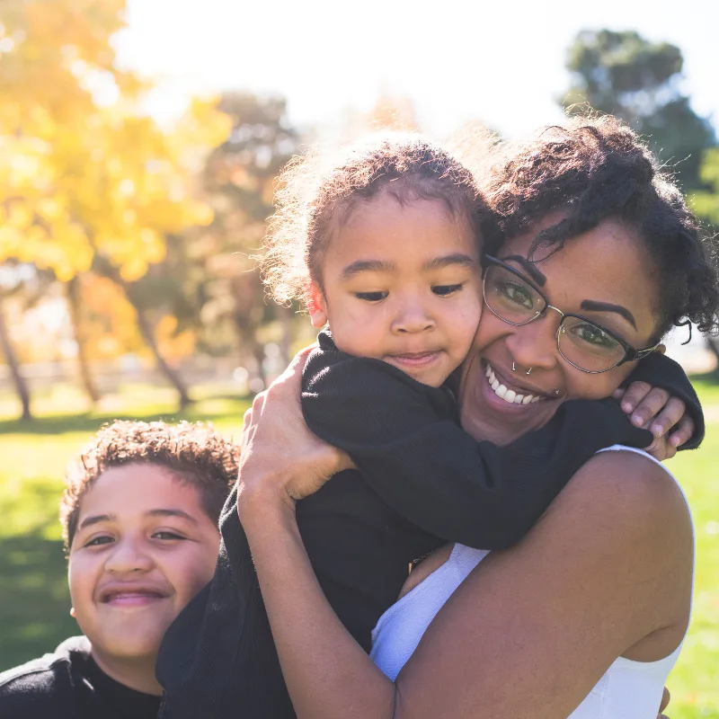 A mother hugging her two children in a sunny park, representing the family protection that chronic illness coverage provides
