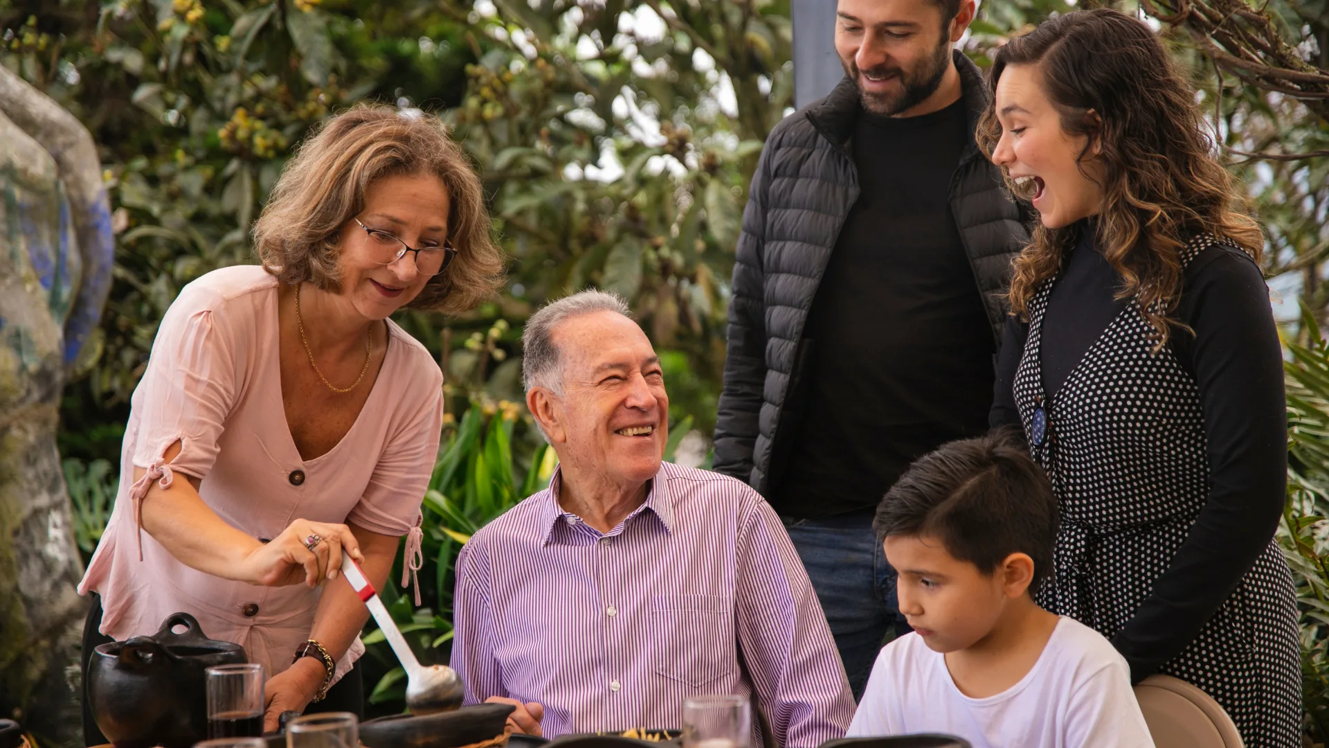 A multi-generational family gathering together outdoors, grandparents, parents, and children sharing a warm joyful moment