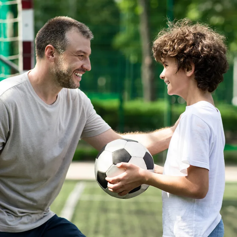A father and son playing with a soccer ball outdoors, representing the active life that disability income protection helps secure