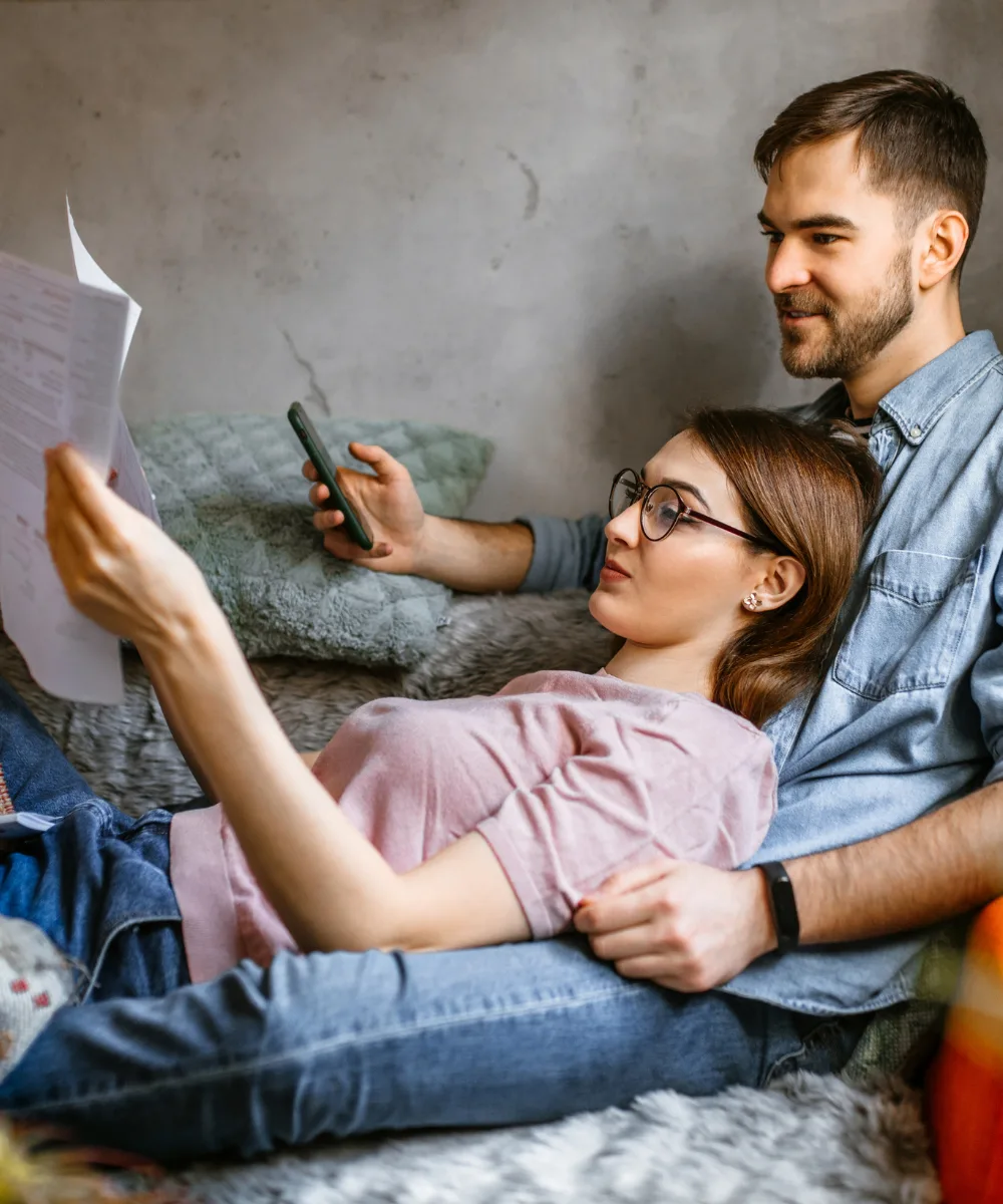 A couple reviewing papers together on a couch, representing the predictable premiums of whole life insurance